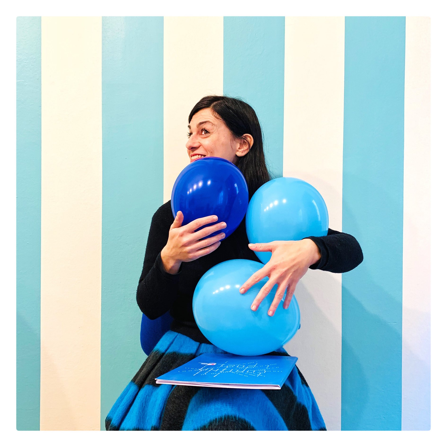 DOCCOMTeam_Design Lucia Portesi del team Design di DOC-COM con palloncini blu e il catalogo di Cortina in mano